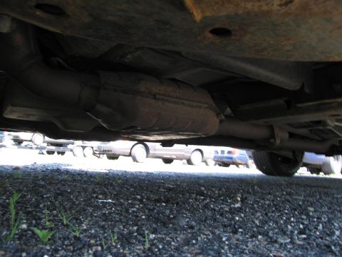 1991 Ford LTD Crown Victoria - The underside of a vehicle is captured, revealing its exhaust components and other cars parked nearby.