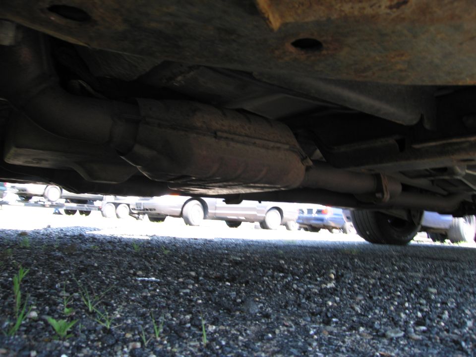 Undercarriage of a vehicle showing exhaust system and catalytic converter, with other vehicles visible in the background