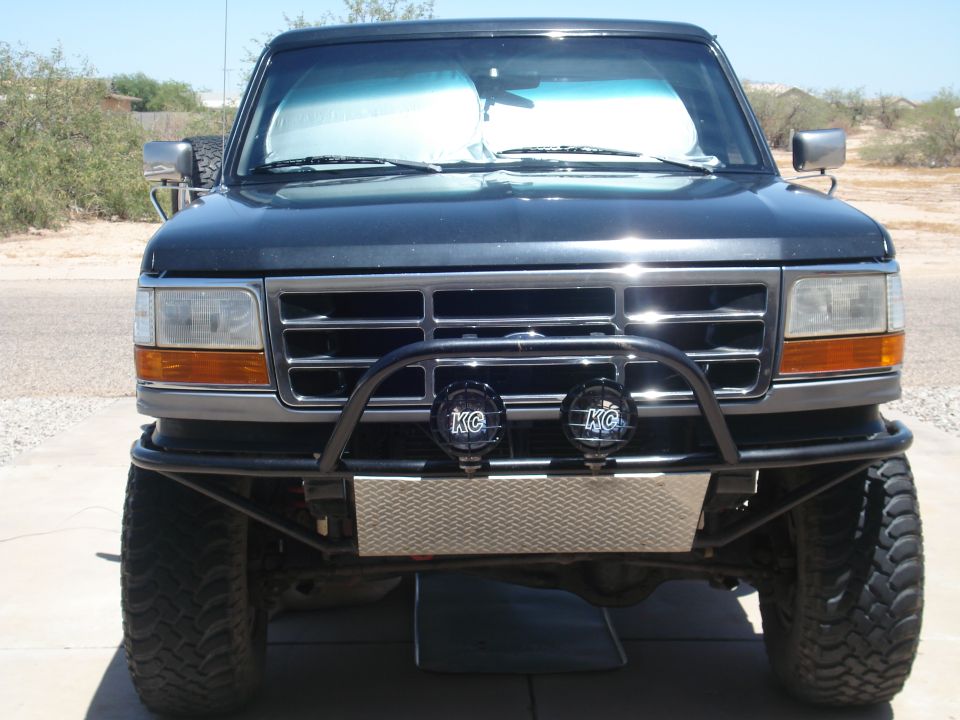 Dark blue Ford Bronco front view, lifted suspension, aftermarket bumper with lights, daytime