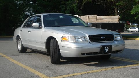 2000 Ford Crown Victoria - Silver Ford Crown Victoria parked in a lot, viewed from the front three-quarter with the Ford oval on the chrome-trimmed grille and a New Y…