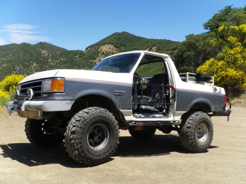 1991 Ford Bronco - Modified 1991 Ford Bronco with large tires and off-road cage, parked outdoors.