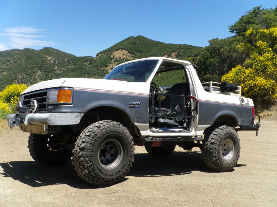 1991 Ford Bronco modified for off-roading, driver's door open, parked on dirt road