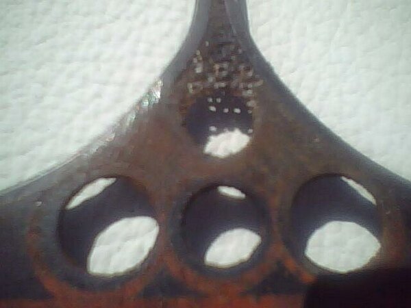 Rusty metal grille emblem with three circular cutouts and visible text