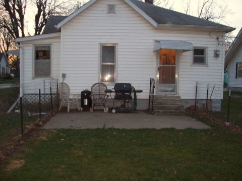 2006 Ford E350 - A view of a residential backyard with a patio, grill, and seating area in front of a white house.