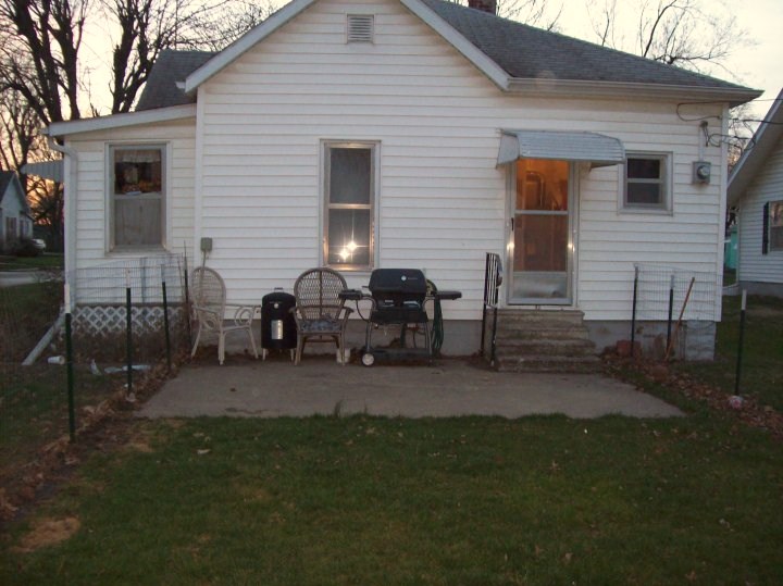 Backyard patio with a white house, chairs, and a grill