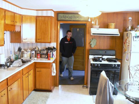 2006 Ford E350 - Interior view of a kitchen wooden cabinetry, a stove, and a person standing in an adjacent doorway.