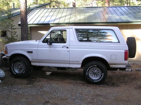 1993 Ford Bronco - Side view of a white 1993 Ford Bronco parked in front of a house with a metal roof.