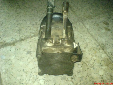1998 Ford Crown Victoria - A car's AC compressor sits on a speckled floor, showing its main body and two connecting pipes.