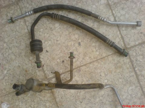 1998 Ford Crown Victoria - pair of air-conditioning refrigerant hoses with a metal mounting bracket and suction line manifold laid on a tile floor.
