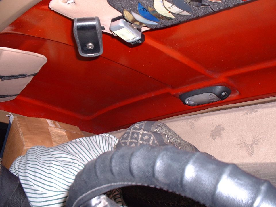 View of the ceiling and a steering wheel inside a vehicle. There are some items on the ceiling and a box and blankets in the back
