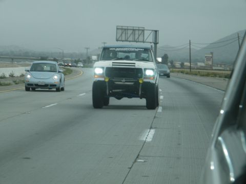 1982 Ford Bronco - A white Ford Bronco with a lifted suspension and large tires drives down a highway under an overcast sky.
