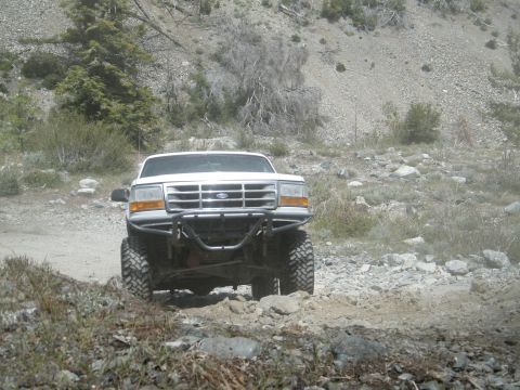 1982 Ford Bronco - A white Ford truck navigates a rocky, off-road path in a dry, mountainous area.