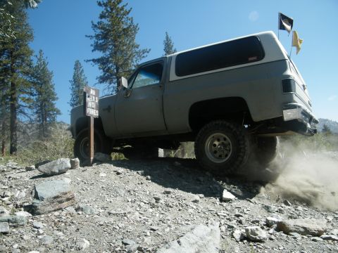 1982 Ford Bronco - This SUV is navigating a steep, rocky incline under a clear blue sky.