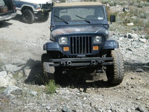 1982 Ford Bronco - A dark blue Jeep Wrangler navigates a rough, rocky terrain on an off-road trail.