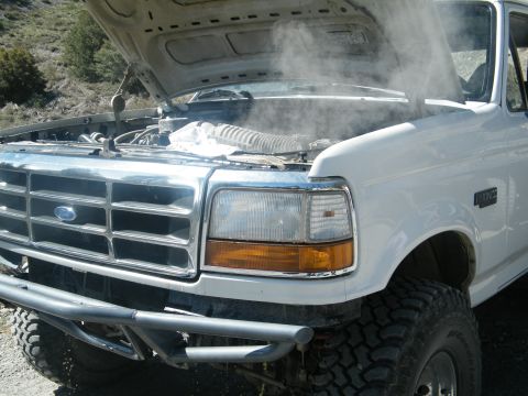 1982 Ford Bronco - White Ford truck with hood open, emitting steam, an aftermarket bumper and off-road tires.