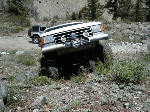1982 Ford Bronco - A white Ford truck navigates a challenging off-road course with another vehicle in the background.