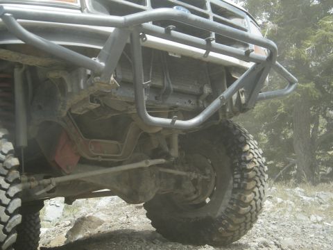 1982 Ford Bronco - Close-up view of the front undercarriage and suspension of a off-road vehicle on a dirt path.