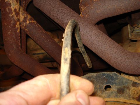 1985 Ford F-150 - A hand holds a bent wiring harness near heavily rusted exhaust pipes, suggesting a need for repair or replacement.