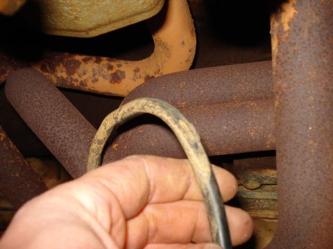 1985 Ford F-150 - Close-up of a hand holding a wire near rusty exhaust pipes, likely under a vehicle.