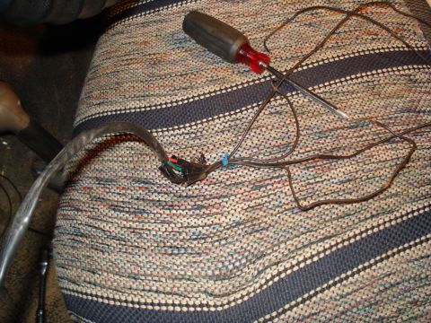 1985 Ford F-150 - A close-up view of a vehicle's wiring harness and a screwdriver resting on a seat cover.