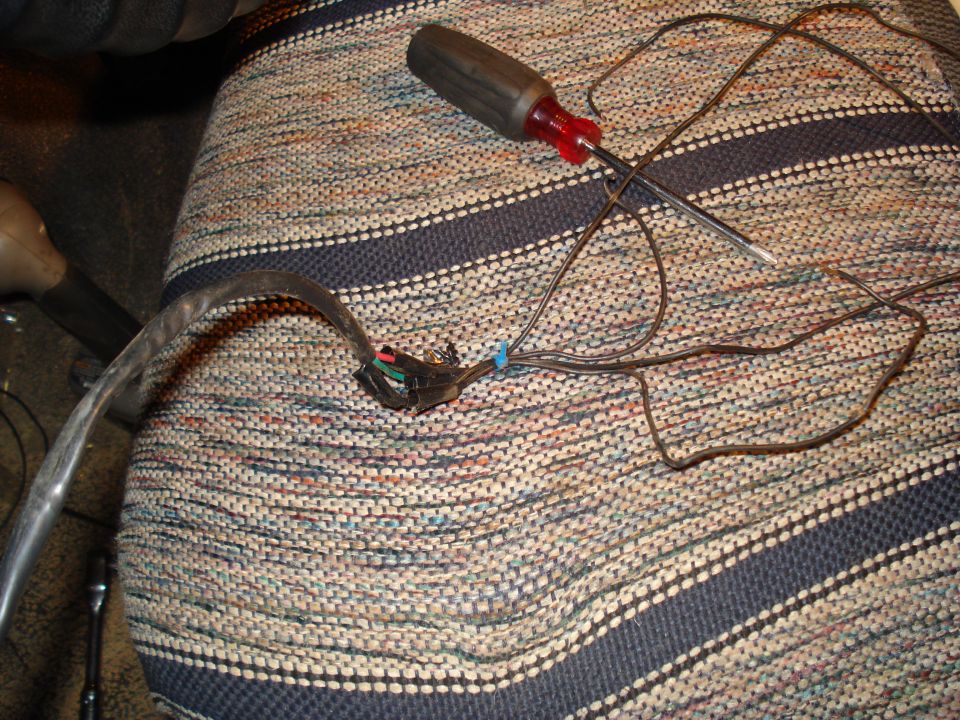 Wiring harness with exposed wires and a screwdriver on a striped fabric seat