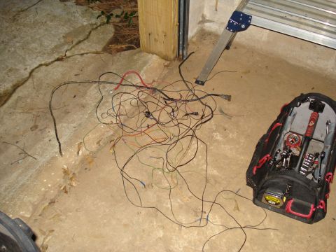 1985 Ford F-150 - A tangled mess of vehicle wiring lies on the ground next to a tool bag and a ladder.