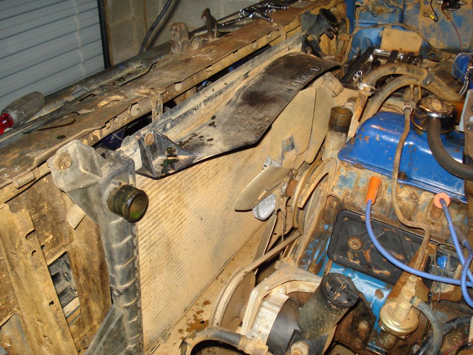 Engine bay showing radiator, fan, and blue valve covers. Some parts are rusty