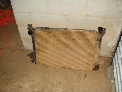 1985 Ford F-150 - A dirty car radiator is shown resting on a concrete floor against a cinder block wall.