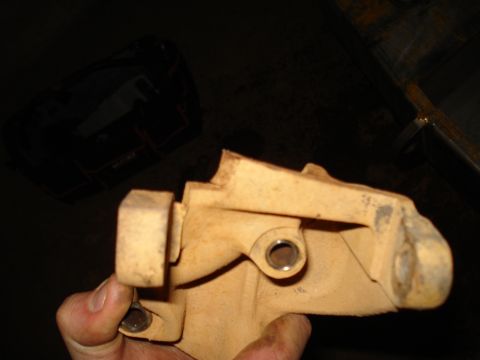 1985 Ford F-150 - A tan metal engine bracket is held in a hand against a dark background.
