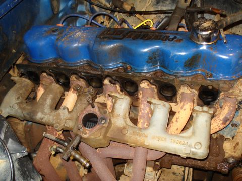 1985 Ford F-150 - Close-up of a Ford V8 engine, showing blue valve covers and exhaust manifolds with visible part numbers.
