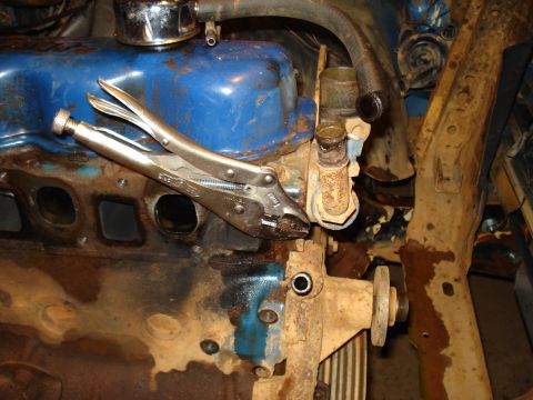 1985 Ford F-150 - Vise grips are clamped onto exhaust manifold bolts on a dirty engine block.