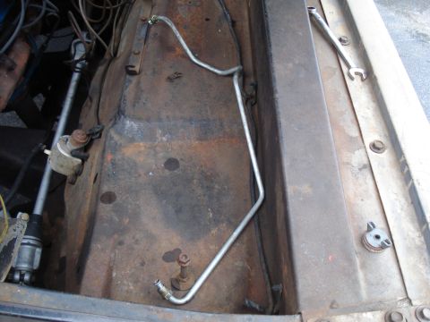 1967 Ford F-250 - The engine bay of a 1967 Ford F-250 shows a metal fuel line and rusty components.