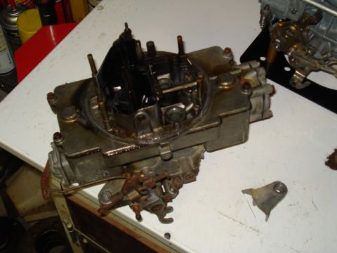 1967 Ford F-250 - A Holley carburetor is shown on a workbench, with a detached metal bracket to its right.