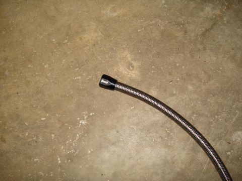 1967 Ford F-250 - A braided fuel line with a black fitting is shown against a concrete background.