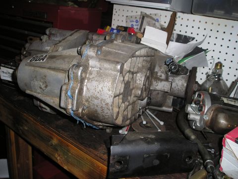 1986 Ford Bronco II - Transfer case assembly with "8GA" sticker, on a workbench with various parts and tools.