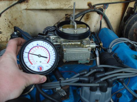 1967 Ford F-250 - A hand holds a fuel pressure gauge connected to a Holley carburetor on an engine.