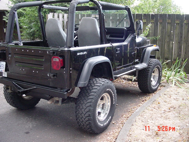 Black Jeep Wrangler with soft-top removed, fender flares and BFGoodrich tires, rear three-quarter view