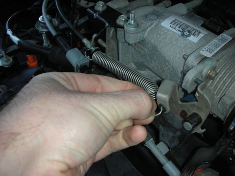 2004 Ford Crown Victoria - Close-up of a hand manipulating a throttle return spring on an engine component.
