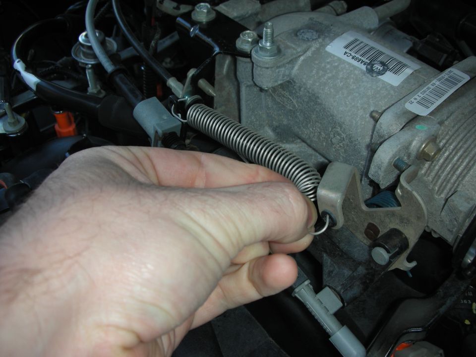Hand holding throttle return spring on metal throttle body assembly with visible barcode sticker