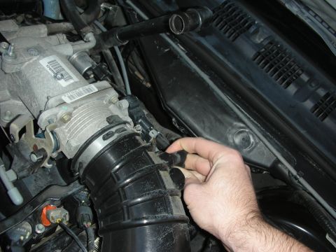 2004 Ford Crown Victoria - Close-up of a hand disconnecting a hose from the air intake assembly, likely during engine maintenance.