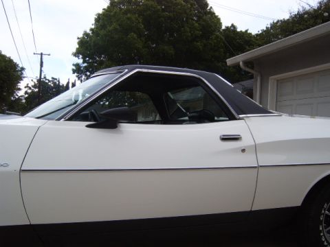 1973 Ford Ranchero - The side profile of a white 1973 Ford Ranchero pickup truck is visible, a black vinyl roof and chrome trim.