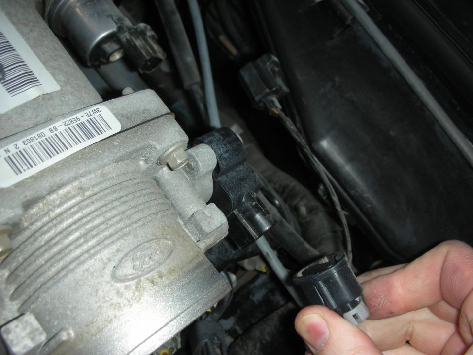 Ford throttle body with part number label and a hand disconnecting a wiring harness