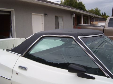 1973 Ford Ranchero - The side profile of a white coupe utility shows its black vinyl top and chrome accents, with a pickup truck visible in the background.