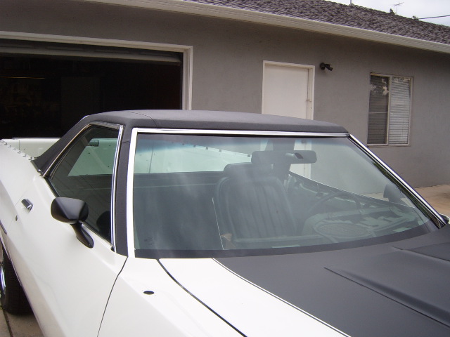 White 1972 Ford Ranchero with black vinyl top and hood stripes, parked in front of a garage