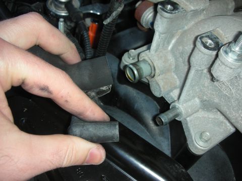2004 Ford Crown Victoria - Close-up of engine components with a hand manipulating a rubber hose near an aluminum intake manifold.