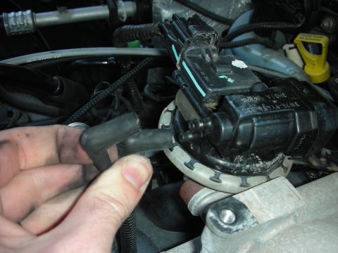 2004 Ford Crown Victoria - Close-up of a hand pulling a spark plug wire boot off a coil pack on a Ford engine, with part number stamped on the coil.