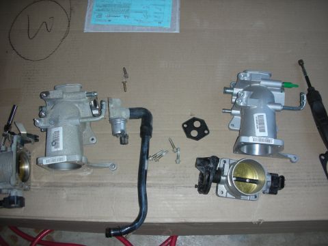 2004 Ford Crown Victoria - Various throttle body and intake manifold components are arranged on a cardboard surface, possibly for installation or comparison.