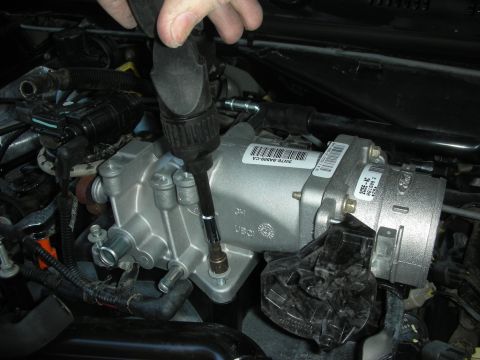 2004 Ford Crown Victoria - A hand uses a socket wrench to install a silver engine component with a Ford logo.