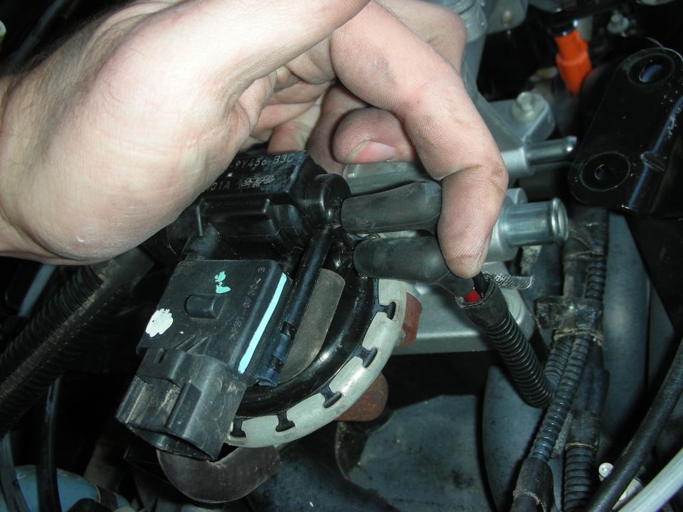Hand disconnecting a black electrical connector from a car engine component