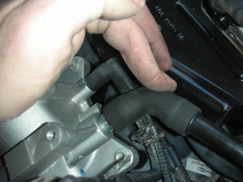 2004 Ford Crown Victoria - A hand is shown installing a black rubber hose onto a silver engine component, likely part of an intake or exhaust system.